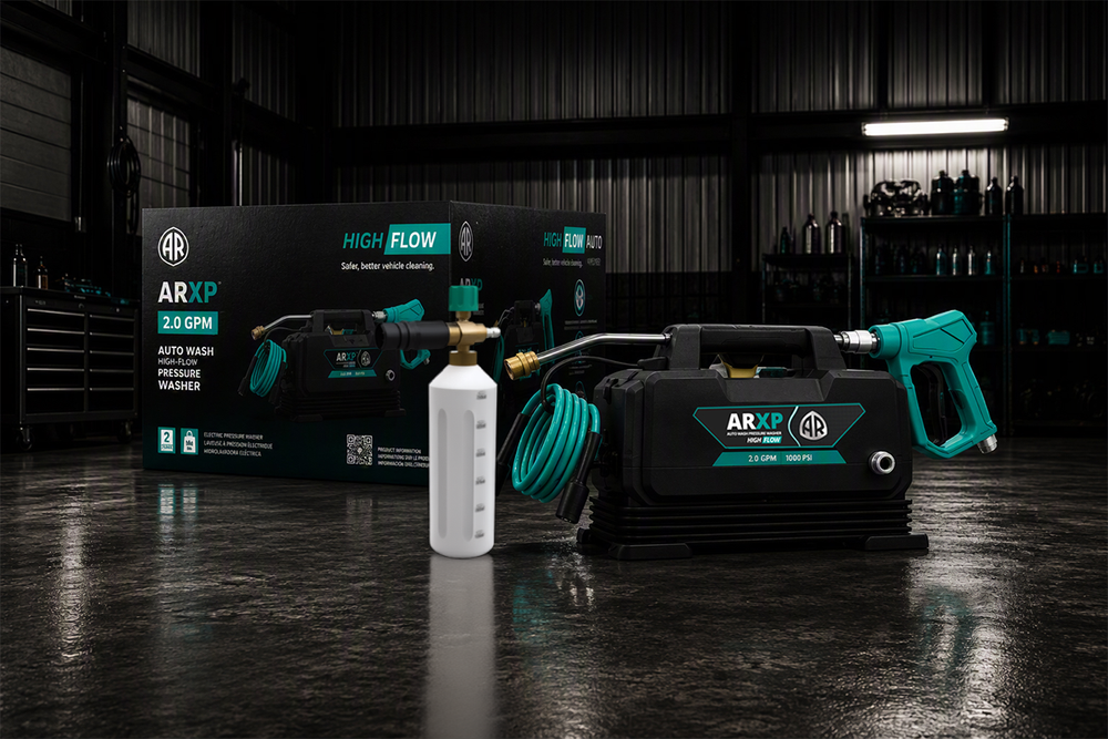 AR XP High Flow 2.0 GPM pressure washer set displayed in a dark workshop environment, featuring the black and teal pressure washer, its matching retail box, a hose, and a white bottle.
